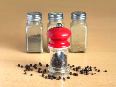 Still life with black peppercorn, hand mills and glass spice jars on wooden surface. Photo closeupの写真素材