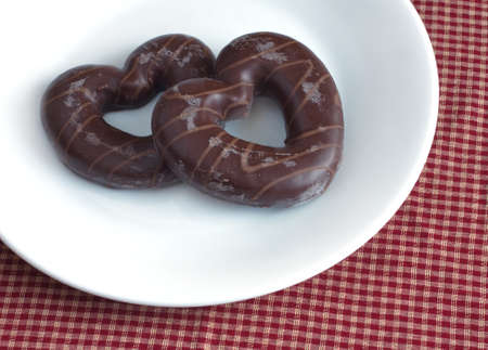 Tasty Valentines Day. Valentines Day. Pastries. Two chocolate covered biscuits in the shape of hearts on a white plate on the red checkered tableclothの写真素材