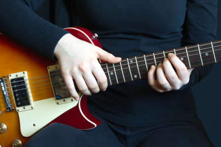 Girl musician plays rock on color six strings electric guitar. Front view closeup