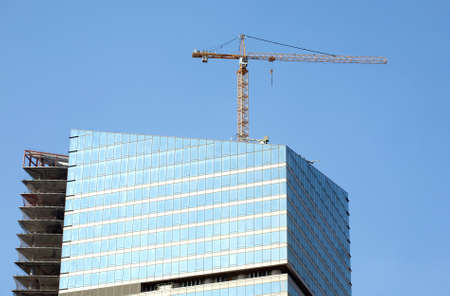 Yellow hoisting tower crane on top of construction skyscraper building over blue skyのeditorial素材