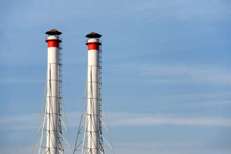 Two high white industrial smoke pipes over clear blue sky horizontal view close upの写真素材