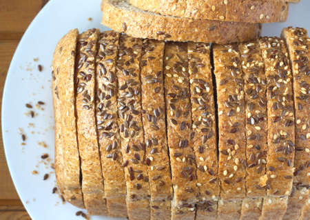 Sliced wholegrain black bread lies on white plate, top view closeup