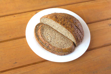Sliced round shape wholegrain bread lies on white plate on brown wooden surface. Photo closeupの写真素材