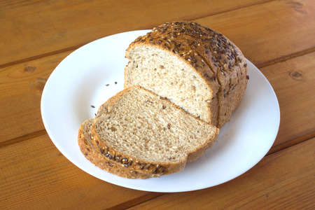 Sliced wholegrain bread lies on white plate on brown wooden surface. Photo closeupの写真素材