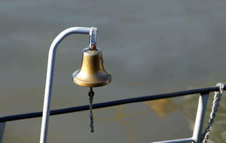 The copper bell on board. The ship bell on a background of calm river water. Horizontal photoの写真素材