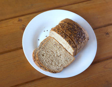 Sliced wholegrain bread with sesame lies on white plate on brown wooden table. Photo closeupの写真素材