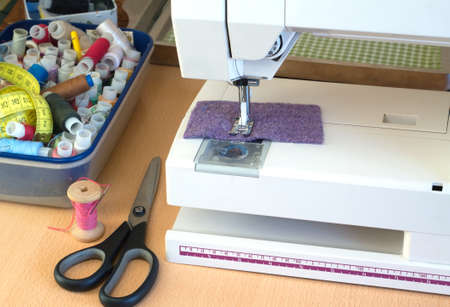 Electric sewing machine and sewing accessories: scissors color spools with thread and cloth closeup