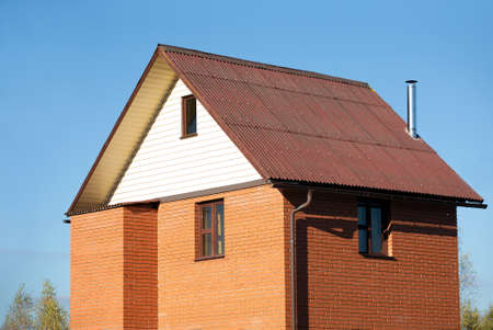 New country house of red brick, brown roof covered and siding on the front and a metal chimneyのeditorial素材