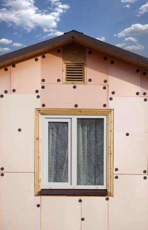 Front view top section and roof of a country house covered with brown metal tile and wall with...