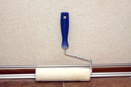 Paint rollers with plastic blue grip, stands in a room at baseboard on the floor near wall, covered with decorative plaster. closeup viewの写真素材