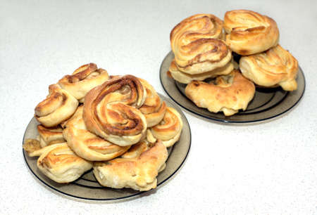 Lots of tasty appetizing baked sweet buns with a crispy ruddy crust on the plates on the table in the kitchenの写真素材