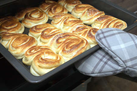 Hostess open oven door and takes the finished crunchy cakes holding tray with oven mitt. Side view...