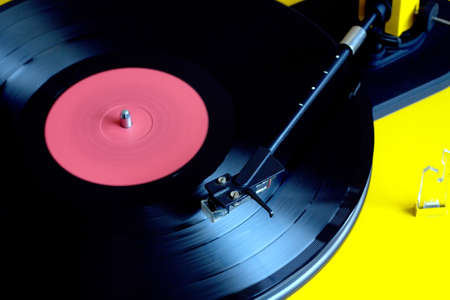 Turntable in yellow case playing a vinyl record with red label. Top view closeupの写真素材