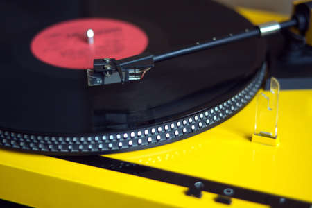 Turntable in yellow case playing a vinyl record with red label. Side view closeupの写真素材