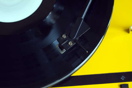 Turntable in yellow case with black tonearm playing a vinyl record with white label. Horizontal photo top view closeupの写真素材