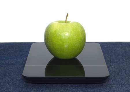 Tasty green apple on kitchen scales on table covered jeans cloth against white background. Front view closeupの写真素材