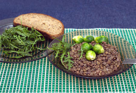 Dietary vegetarian breakfast. Lentils, broccoli and arugula salad leaves with grain bread on a plates on a straw mat in the kitchen. Photo closeupの写真素材