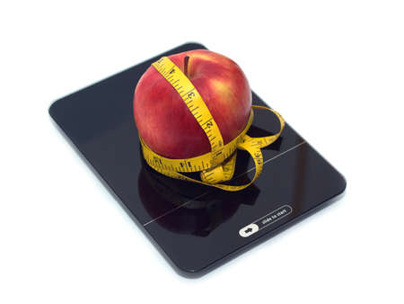 Slide to start new life! Large tasty red apple on kitchen scales and measuring tape isolated on white background. Side view closeupの写真素材