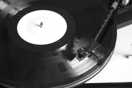 Turntable in silver case playing a vinyl record with white label. Horizontal photo top view closeup