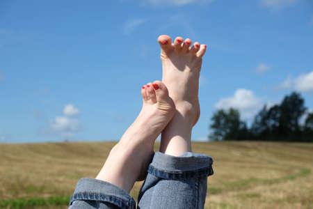 Beautiful playful female bare feet with red nails in rolled blue jeans close-up against summer...