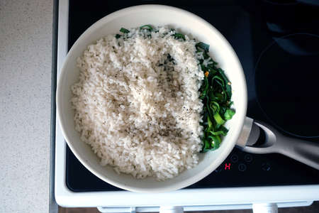 White rice prepared spice and fried leek in big kitchen pan with handle on modern electric stove top view closeupの写真素材