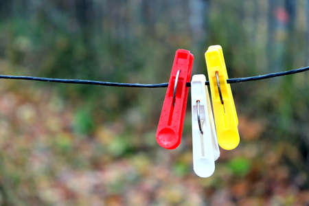 Three colored clothespins hanging on black rope on a blurred background in autumn day outdoors horizontal view closeupの写真素材