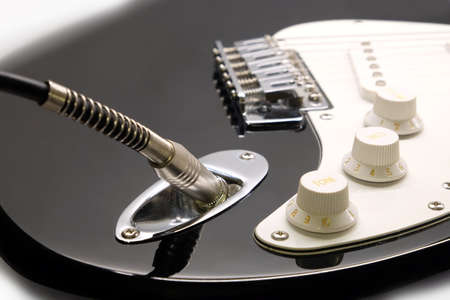 Part of modern electric six string guitar black color with glossy finish with metal jack in socket, pickups and control knobs isolated on white background horizontal view close upの写真素材