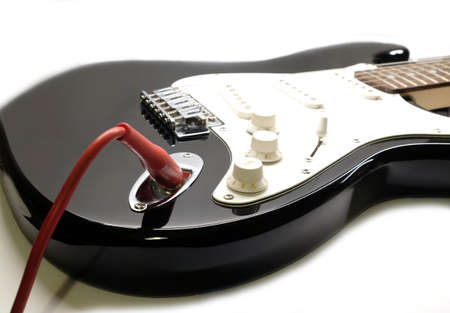 Part of modern electric six string guitar black color with glossy finish with red cord in socket, pickups and control knobs isolated on white background horizontal view close upの写真素材
