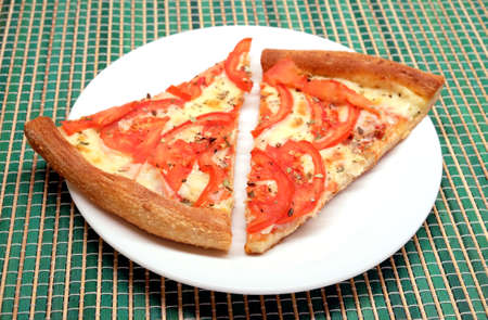 Two appetizing pizza pieces on white plate on green wicker mat closeupの写真素材