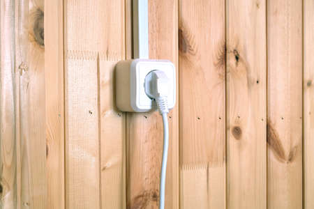 White electric plug in socket on wooden wall with vertical planks side view closeupの写真素材