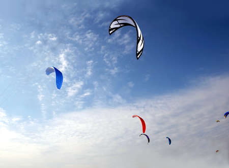 Many big colorful sport kites flying high in bright blue sky on sunny dayの写真素材
