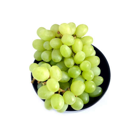 Lot of ripe green grape berries on bunch in black round bowl on white background top view close upの写真素材