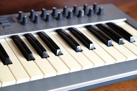 Electronic synthesizer keyboard with many control knobs in silver plastic body on wooden background side view closeupの写真素材