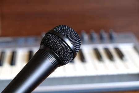 Black vocal microphone close up against defocus electronic synthesizer keyboard with many control knobs in silver plastic body as backgroundの写真素材