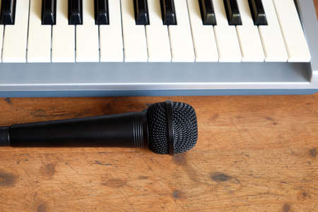 Black voice microphone and electronic synthesizer keyboard in silver plastic body with black and white keys on wooden background front view closeupの写真素材