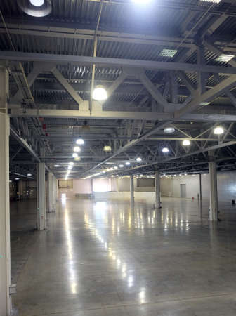 Large empty warehouse interior in an industrial building with high vertical columns and with high ceiling and artificial lightingのeditorial素材