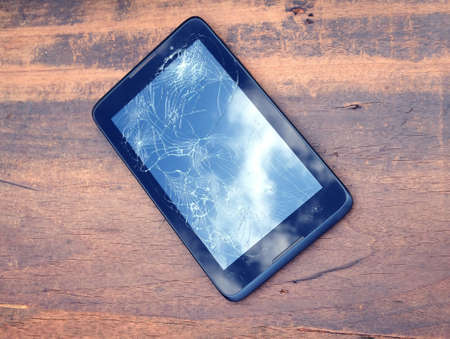 Electronic tablet in black case with broken touch screen on brown wooden background