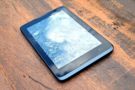 Electronic tablet in black case with broken touch screen on brown wooden backgroundの写真素材