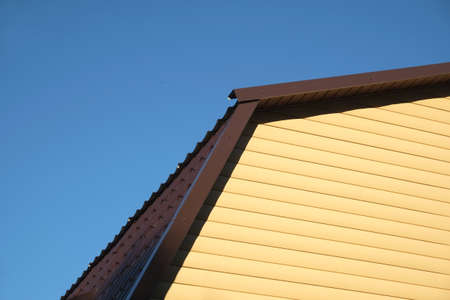 Part of rural house Wall covered with yellow siding and brown metal roof on clear blue cloudless sky...