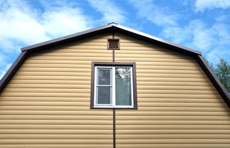 Top section of a modern private country house wall covered with yellow siding and brown metal roof...