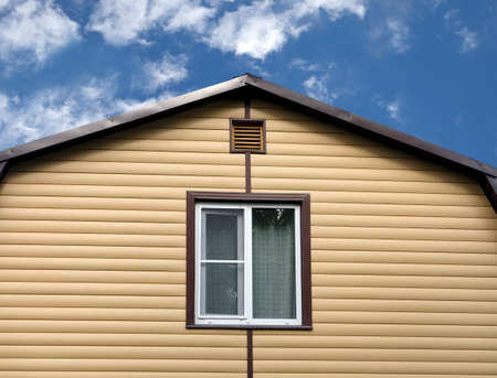 Top section of a modern private country house wall covered with yellow siding and brown metal roof...