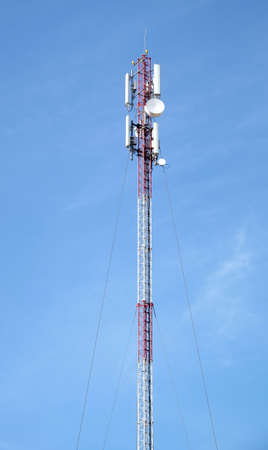 High red and white cellular tower with aerials on top over clear blue sky in sunny day