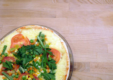 Fragment of cooked appetizing pizza with tomatoes, corn and green peas on a round plate on a wooden background top viewの写真素材