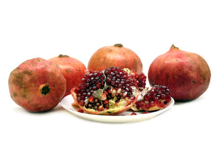 Whole and half pomegranates with ripe seeds on plate isolated on white background front view closeupの写真素材
