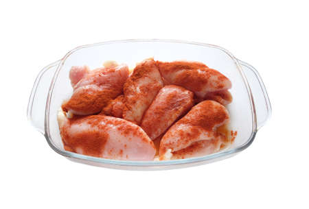 Many raw juicy cutted chicken fillets pink pieces well sprinkled with red pepper inside square transparent bowl isolated on white are ready for baking front view closeupの写真素材