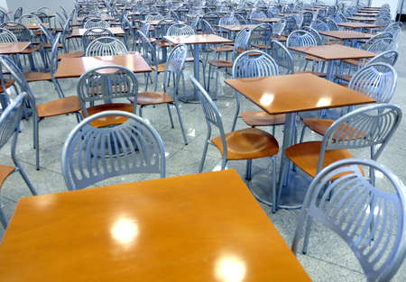 Many brown square eating tables and metal chairs staying in empty cafe hall inside high modern...