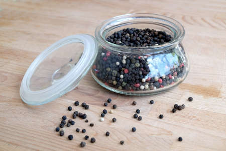 Hot spice ingredients for food. Still life with black pepper seeds inside round glass jar and...