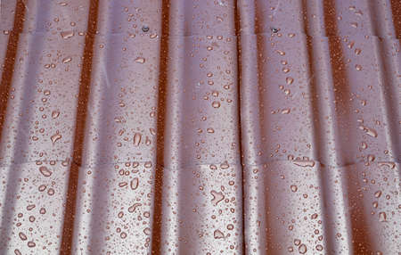 Fragment the wet brown metal roof of the house in the form of roof tiles with many drops after the rain, top view close upの写真素材
