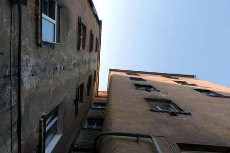 Corner of very old threadbare dwelling house wall view from inner yard bottom up under clear blue sky on sunny dayの写真素材