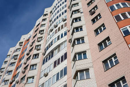 Facade of a large multi-storey block of flats with many apartments over blue sky with light clouds bottom to up viewの写真素材